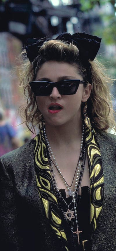 Woman walking towards man wearing 1980s style clothing, sunnies and big hair bow