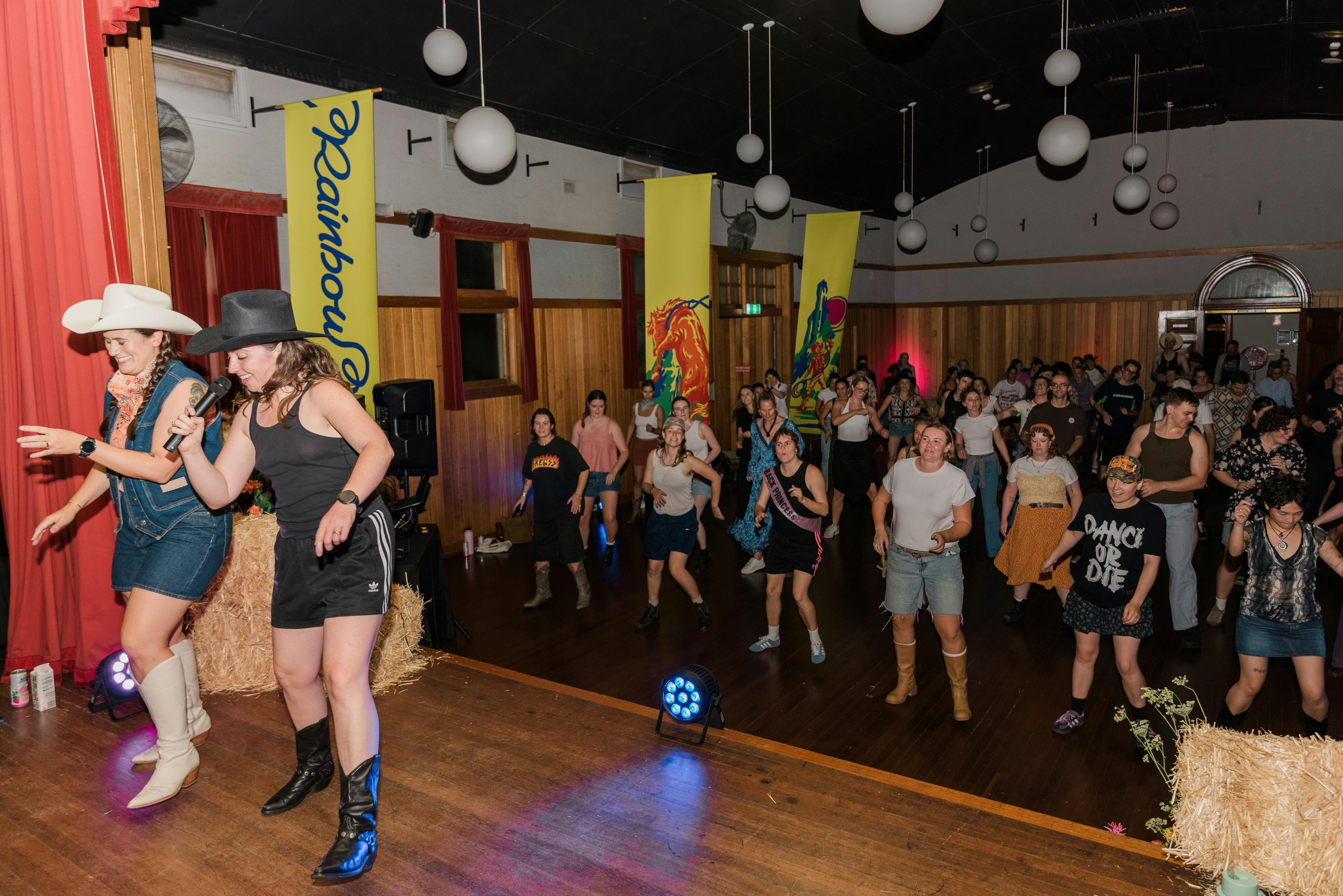 Two people stand on stage teahcing line dancing to an enthusiastic crowd.