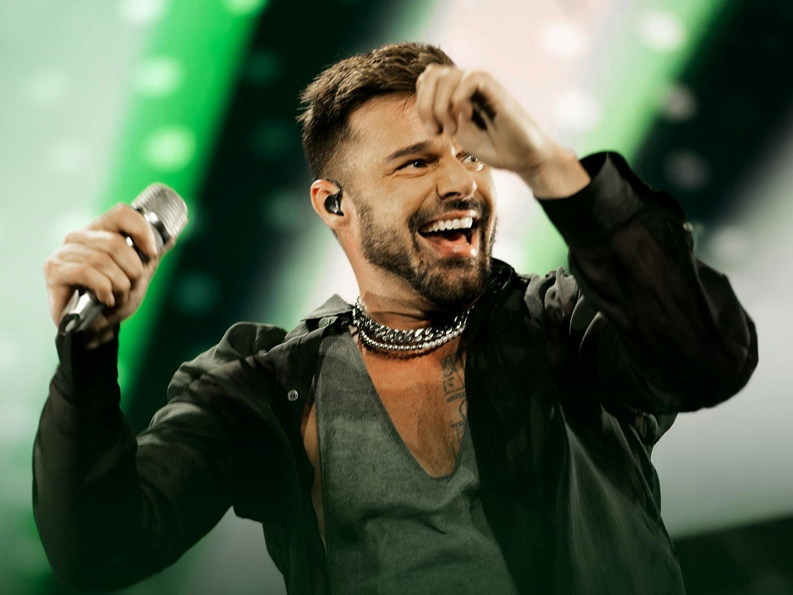 Ricky Martin performing. Mic in hand, green, black, white  background
