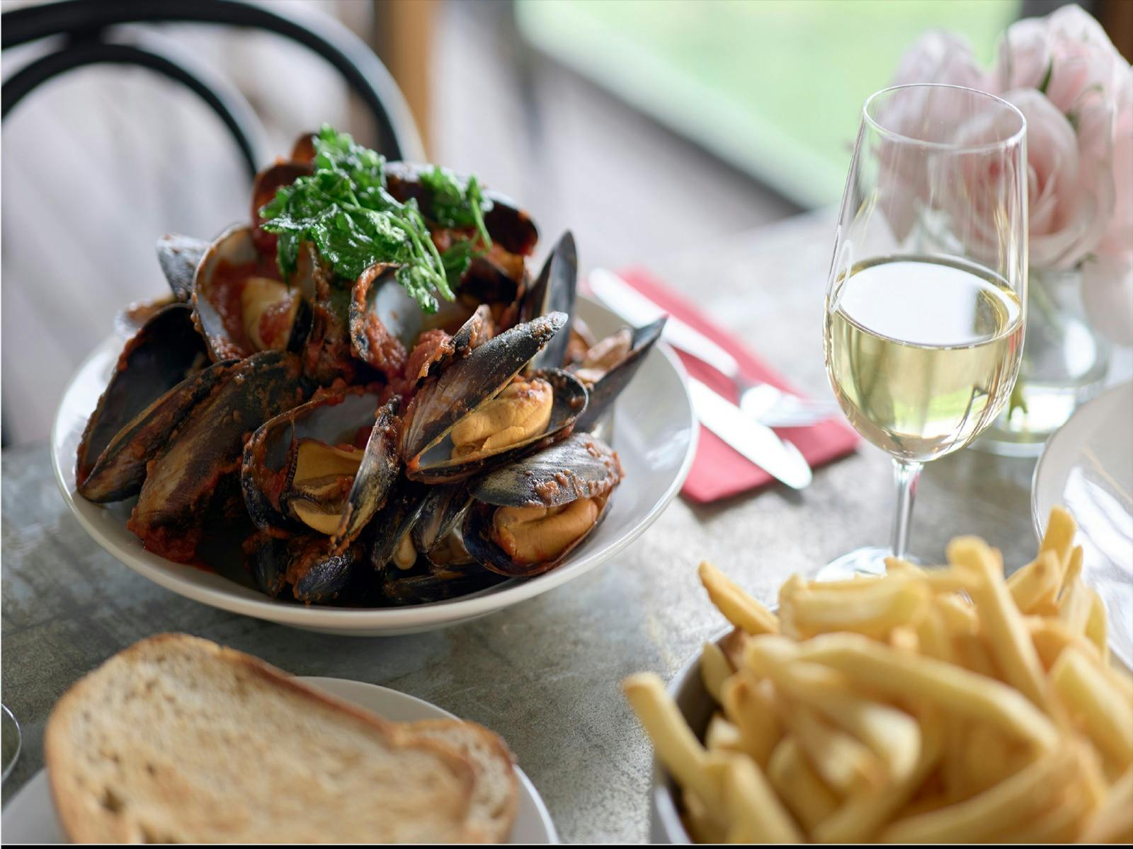 A bowl of mussels with a glass of wine on a timber table