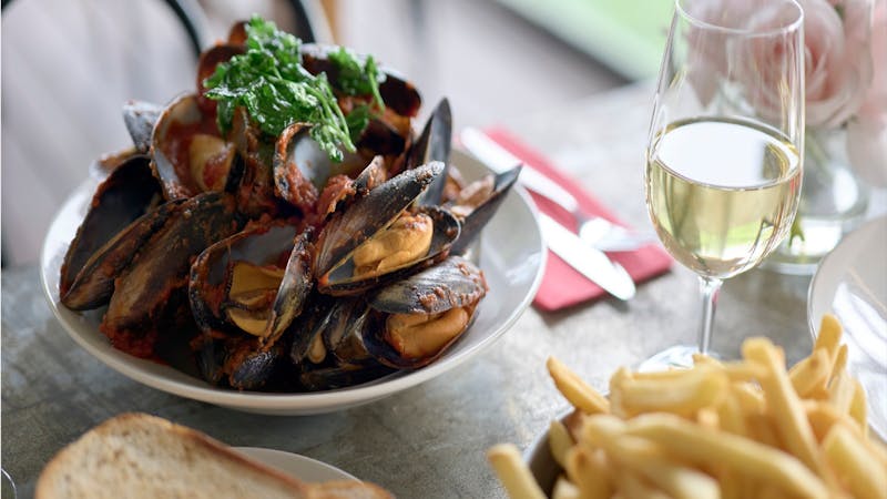 A bowl of mussels with a glass of wine on a timber table