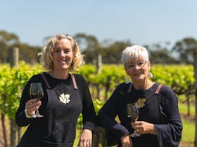 Two ladies standing in a vineyard holding a glass of wine