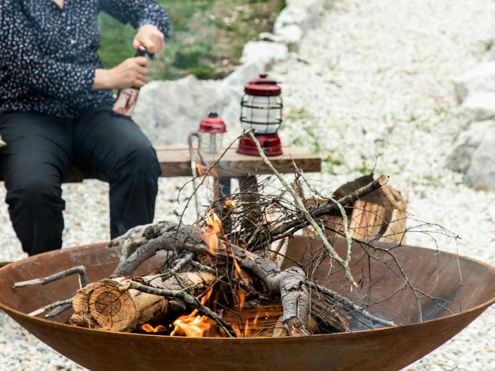 Large steel fire pit with a woman opening a cider behind it