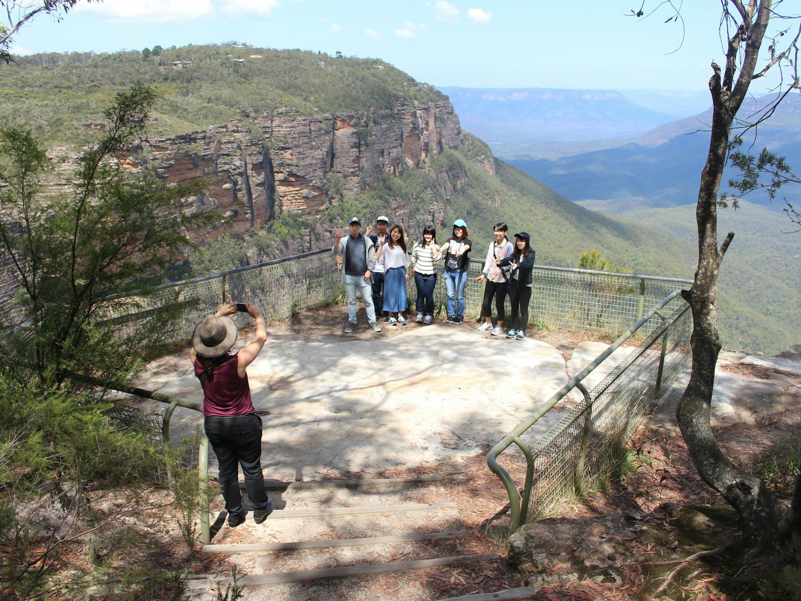 Guide taking photos of a group at a rocky lookout with a deep valley in the background