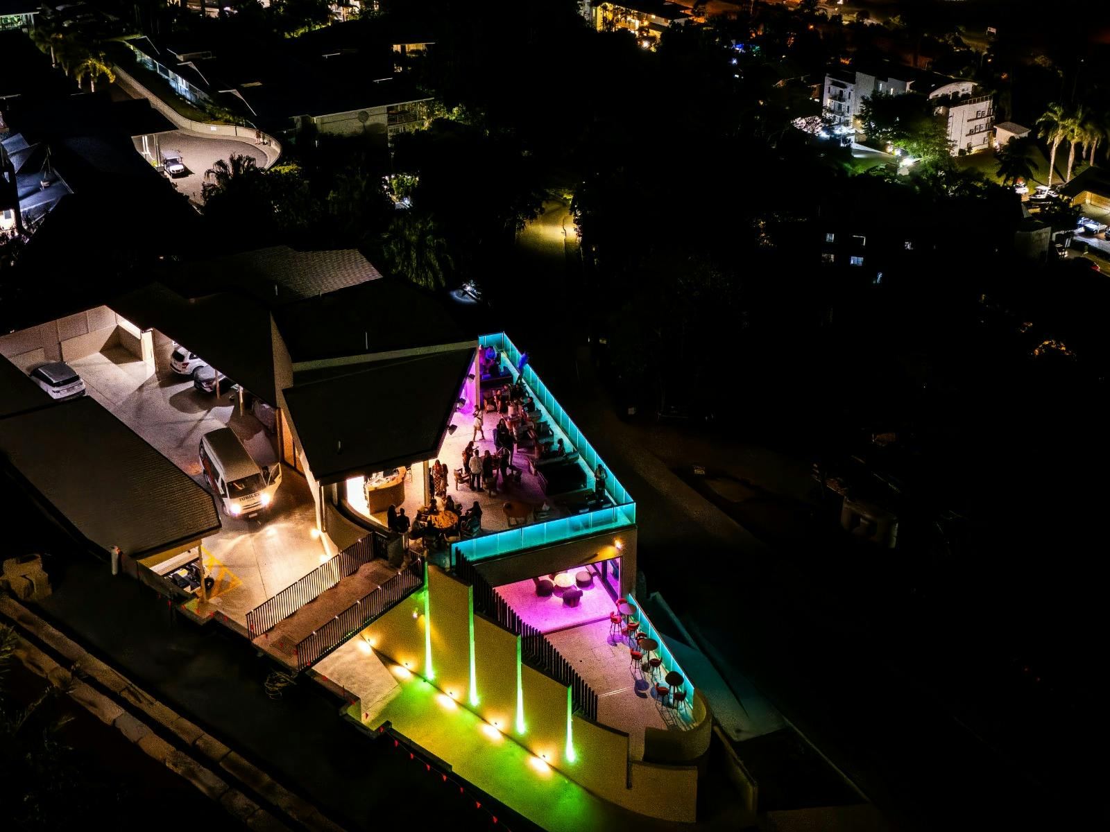 Aerial view of 74 Islands Distillery rooftop at night with guests and colourful lighting.