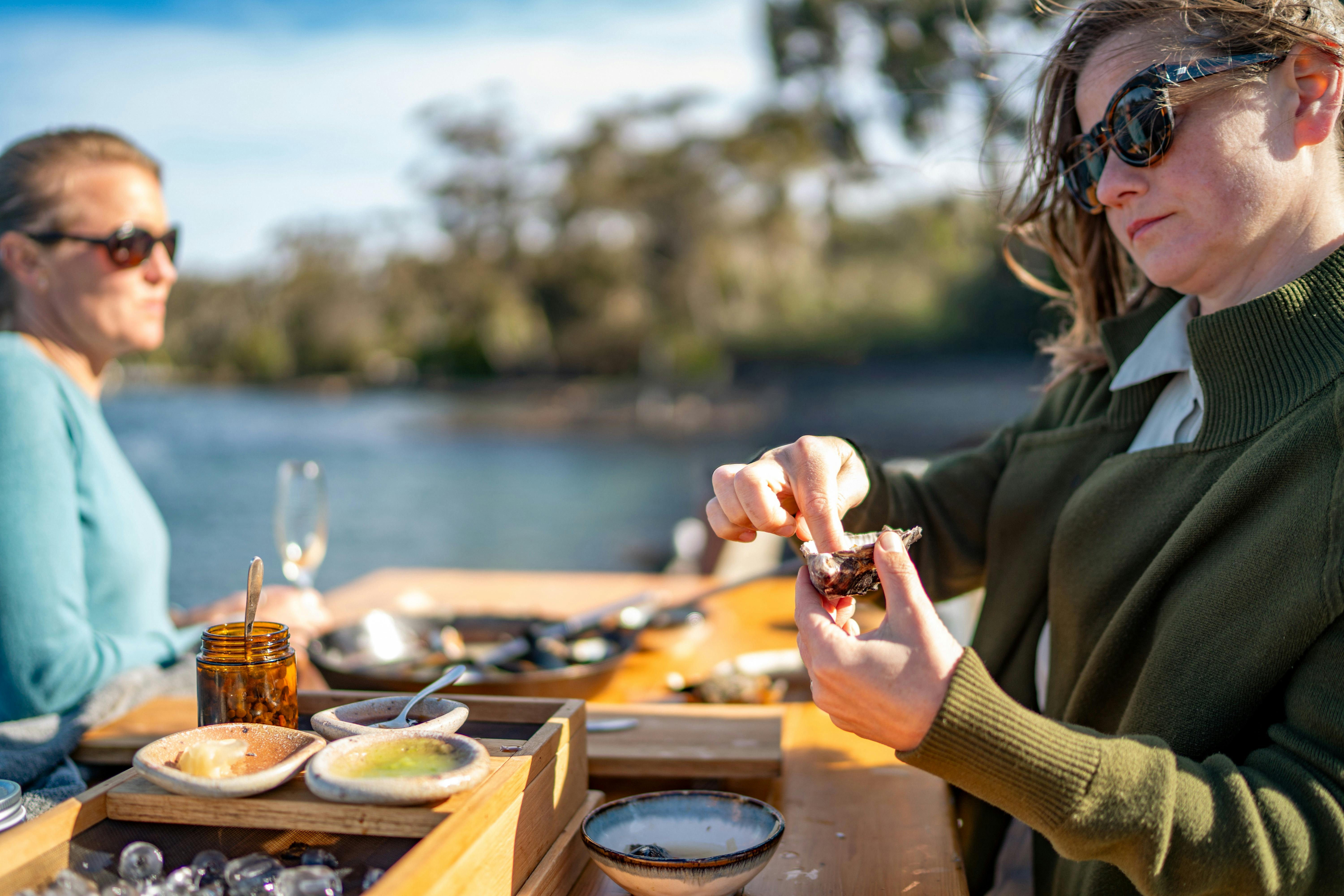 Guests enjoying oyster in afternoon sun with St Helens Bay in the background