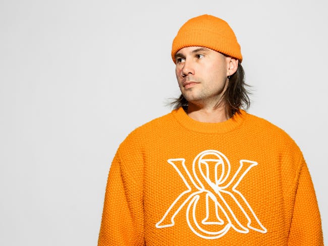 DJ / Producer Torren Foot wearing a orange jumper and beanie on a grey background