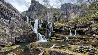 A waterfall leading into a pool of water with some rocks.