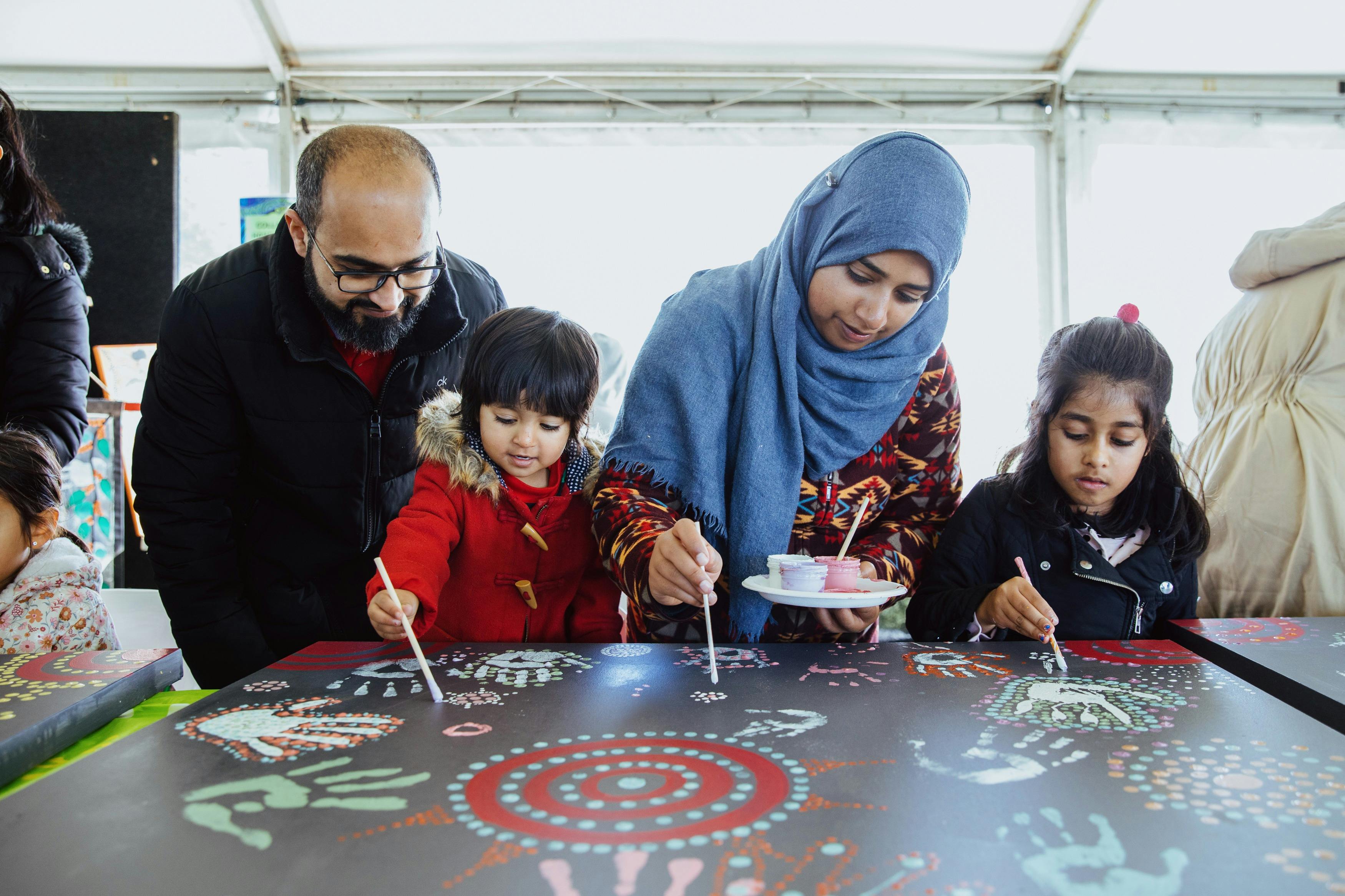 Family of four painting on large canvas decorated with colourful patterns and handprints