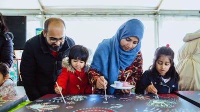 Family of four painting on large canvas decorated with colourful patterns and handprints