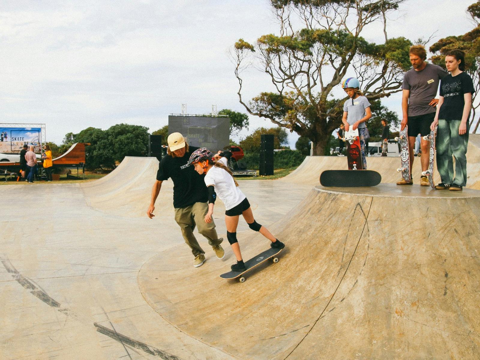 instructor supports a young female skateboarder as she rolls down the ramp