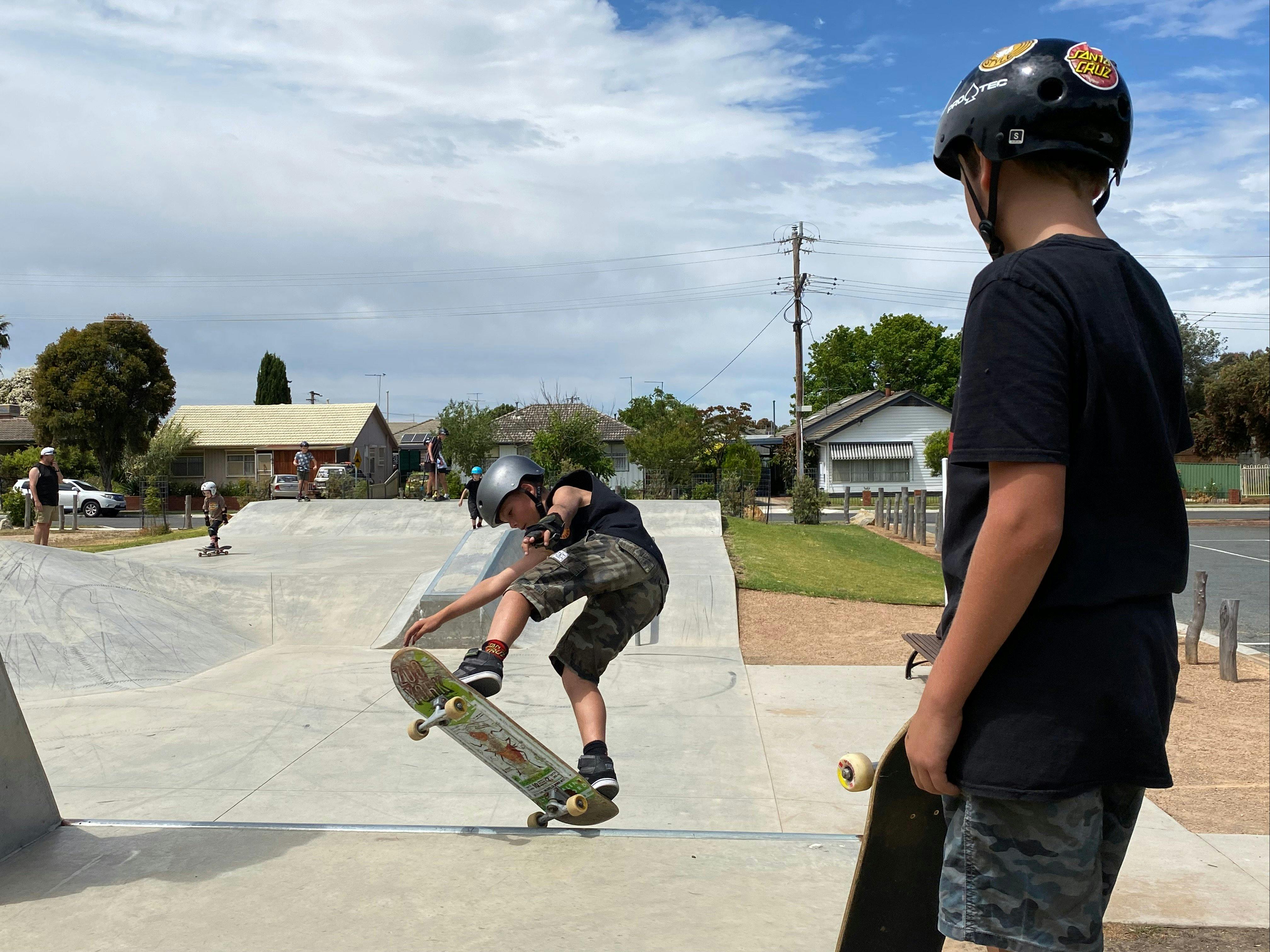 Youth doing a trick on the cement skate park with other youth looking on