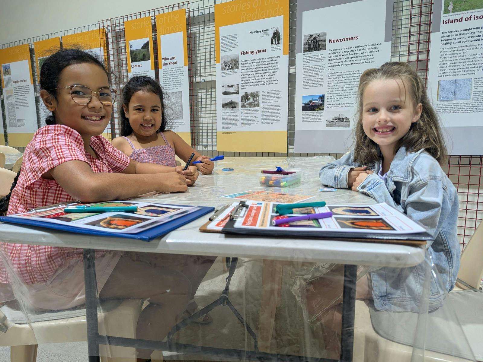 Three children sitting around a table doing craft.
