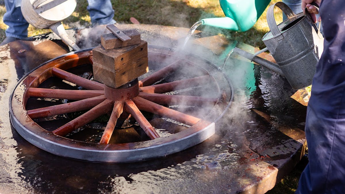 Heated metal wheel rim being cooled by water and being set onto wooden wheel.