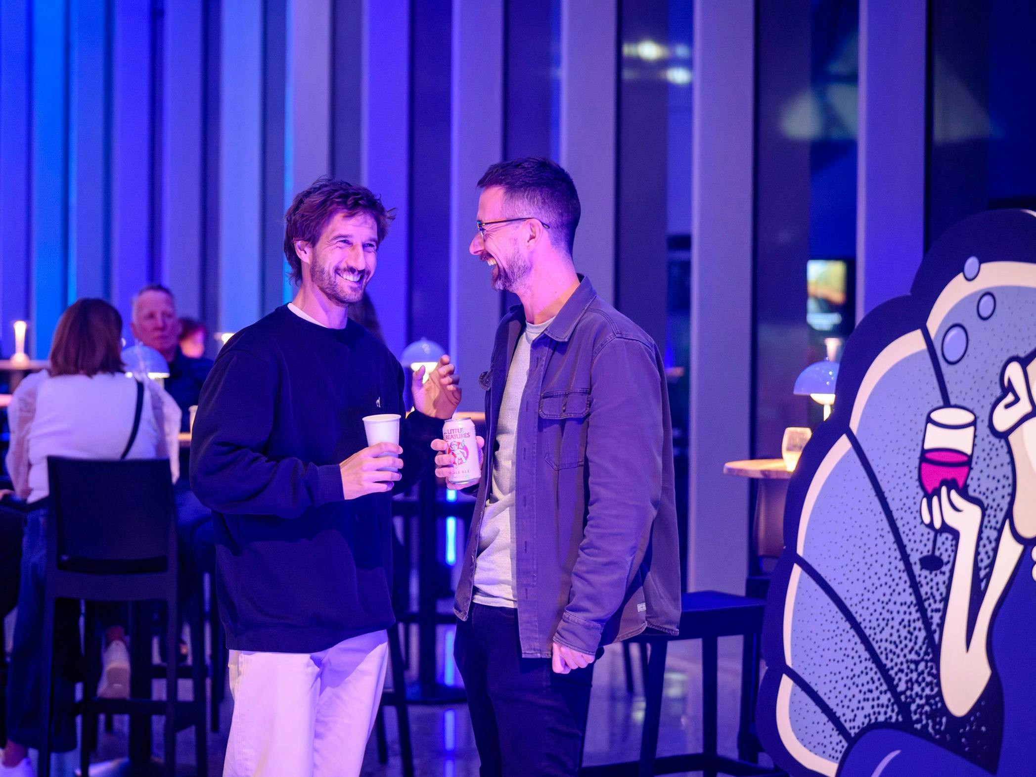 Two men enjoy a drink in an ambient purple-lit room