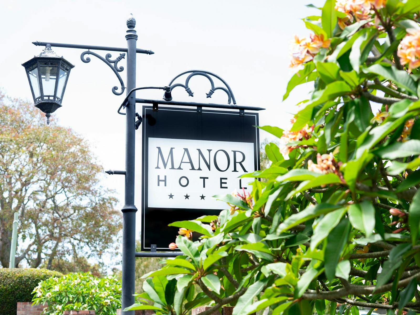 Image of the ornate Ballina Manor sign next to frangipani treesnext