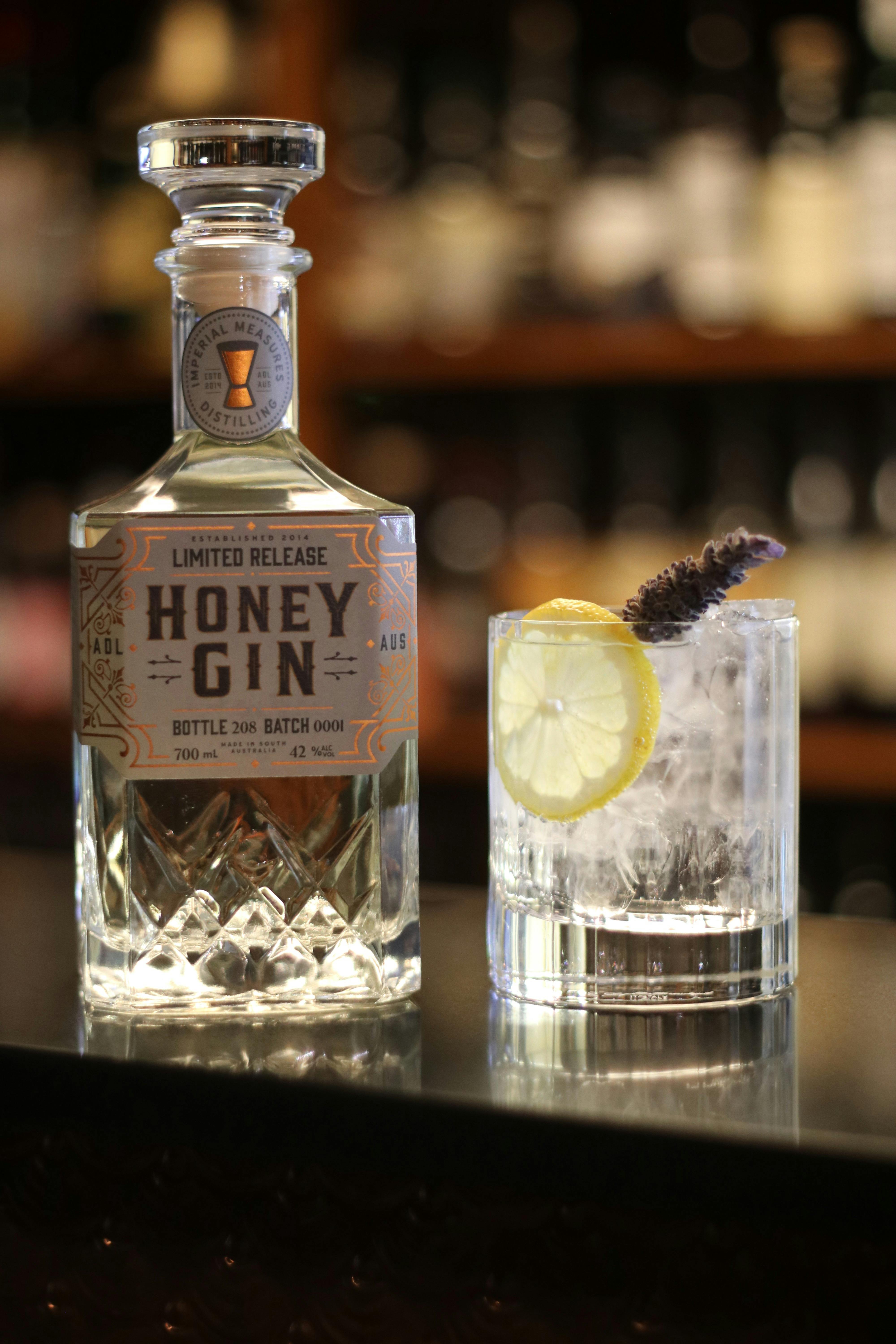 A bottle of Limited Release Honey Gin next to a Gin & Tonic garnished with lavender and fresh lemon