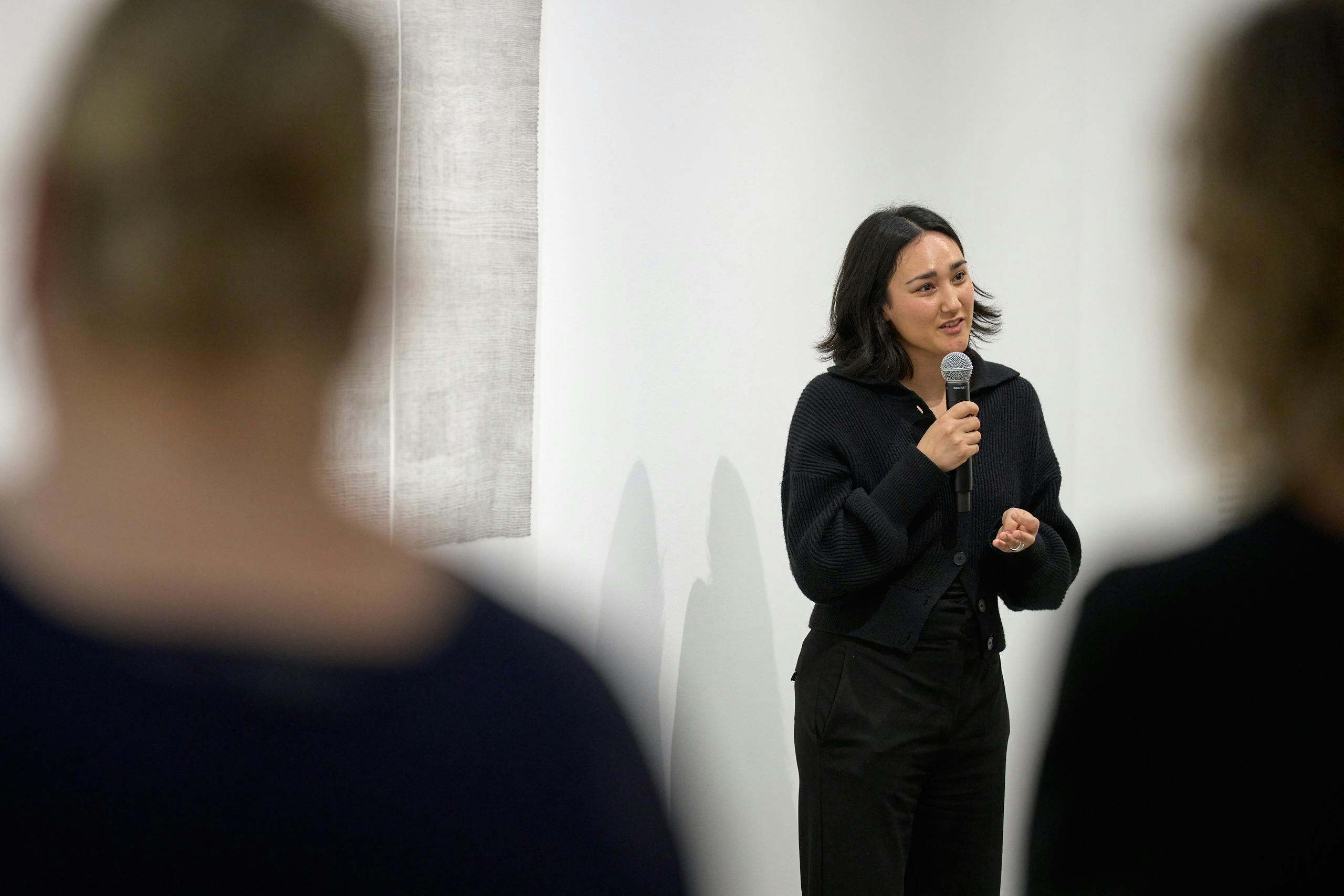 Woman speaking with microphone in front of paper artwork