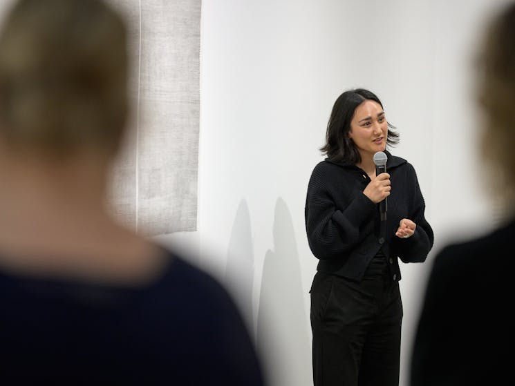 Woman speaking with microphone in front of paper artwork