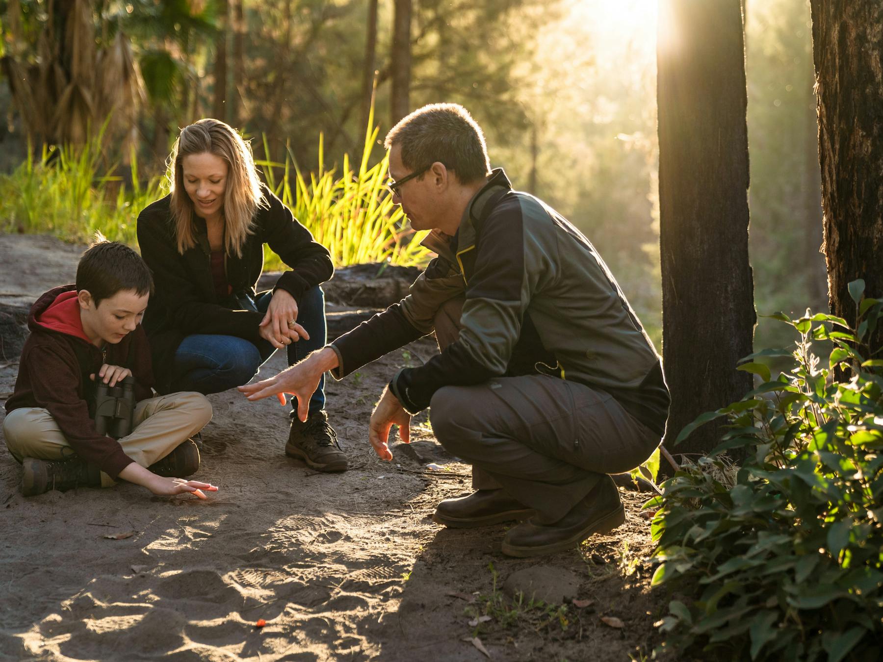 Tour guide and young family crouched down inspecting animal tracks in the sand.