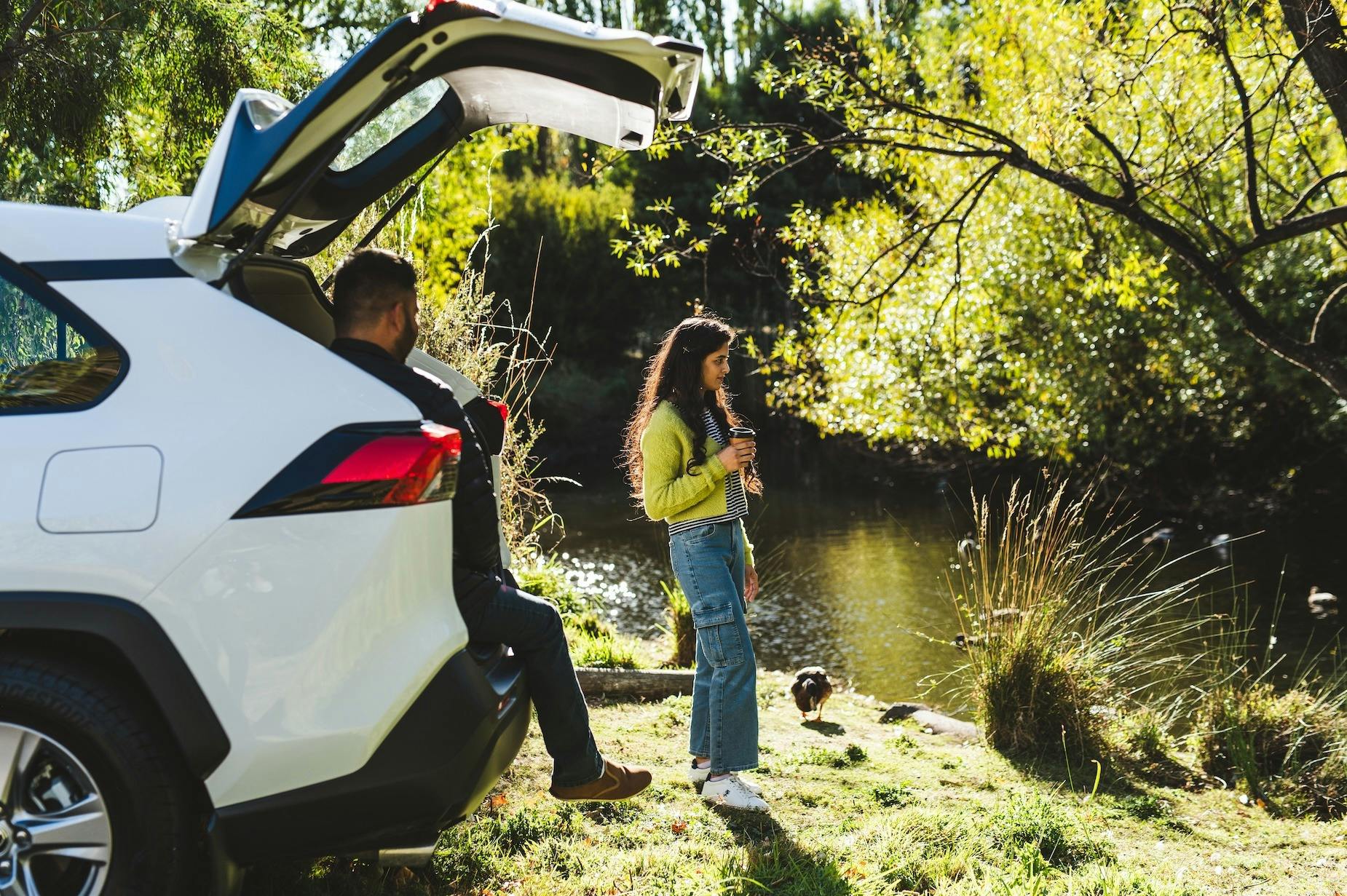 A couple park their car beside a river to watch the ducks in autumn sun