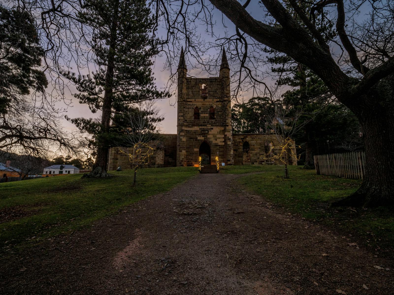 The old Convict Church lit up by some decorative lights, and surrounded by tree branches at dusk