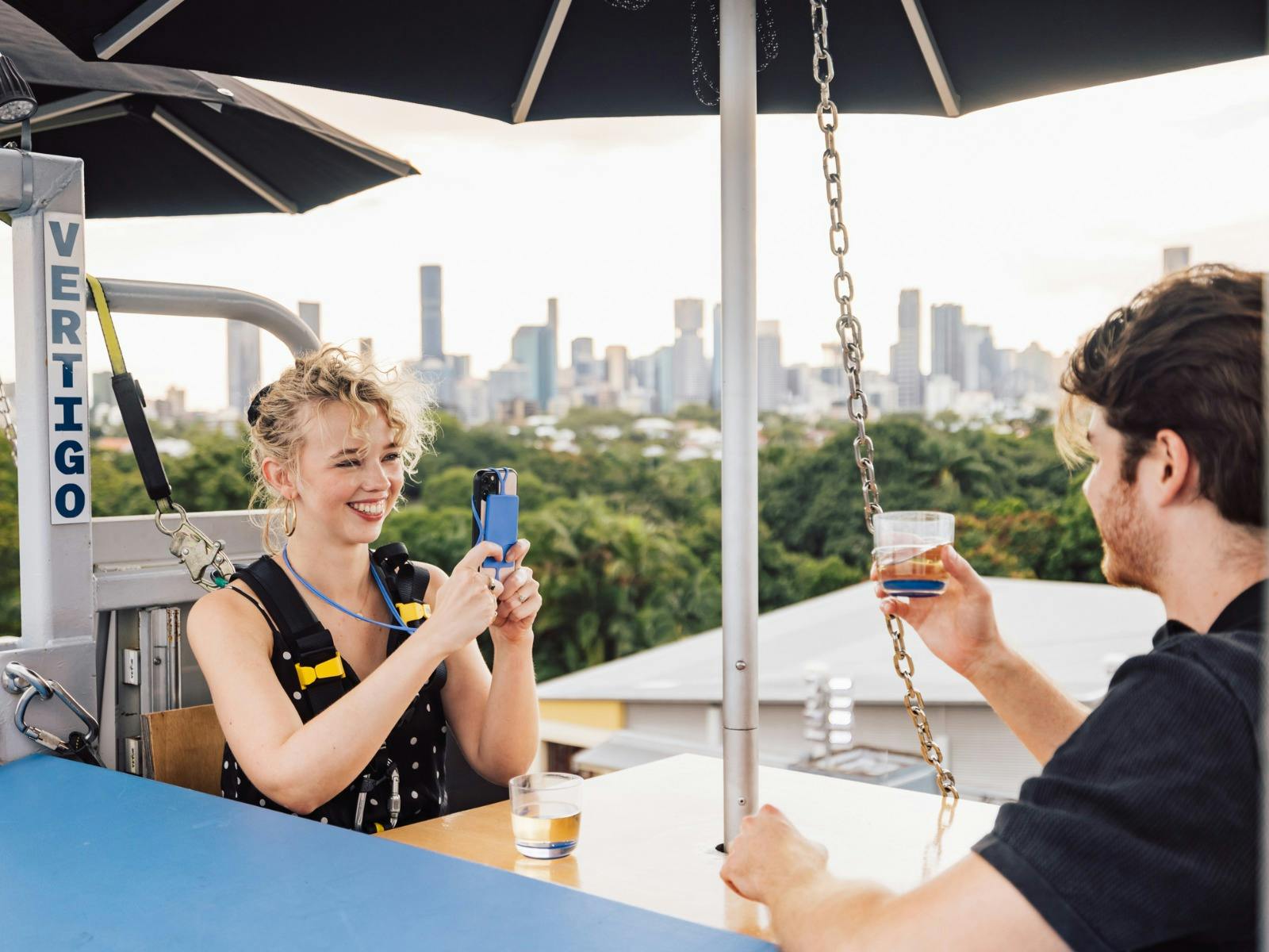 A woman smiles, taking a photo with her phone while sharing drinks with a man at Vertigo. A woman smiles, taking a photo with her phone while sharing drinks with a man at Vertigo.