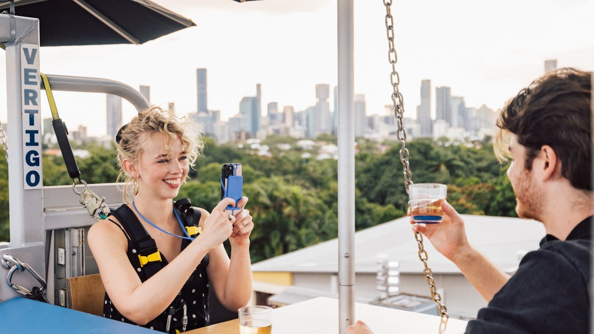 A woman smiles, taking a photo with her phone while sharing drinks with a man at Vertigo.