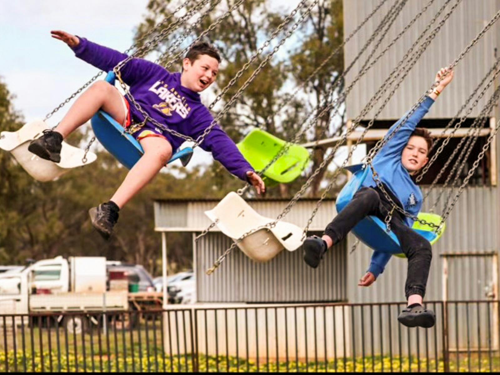 Two children on swings on flying carousel ride at Barellan Show.