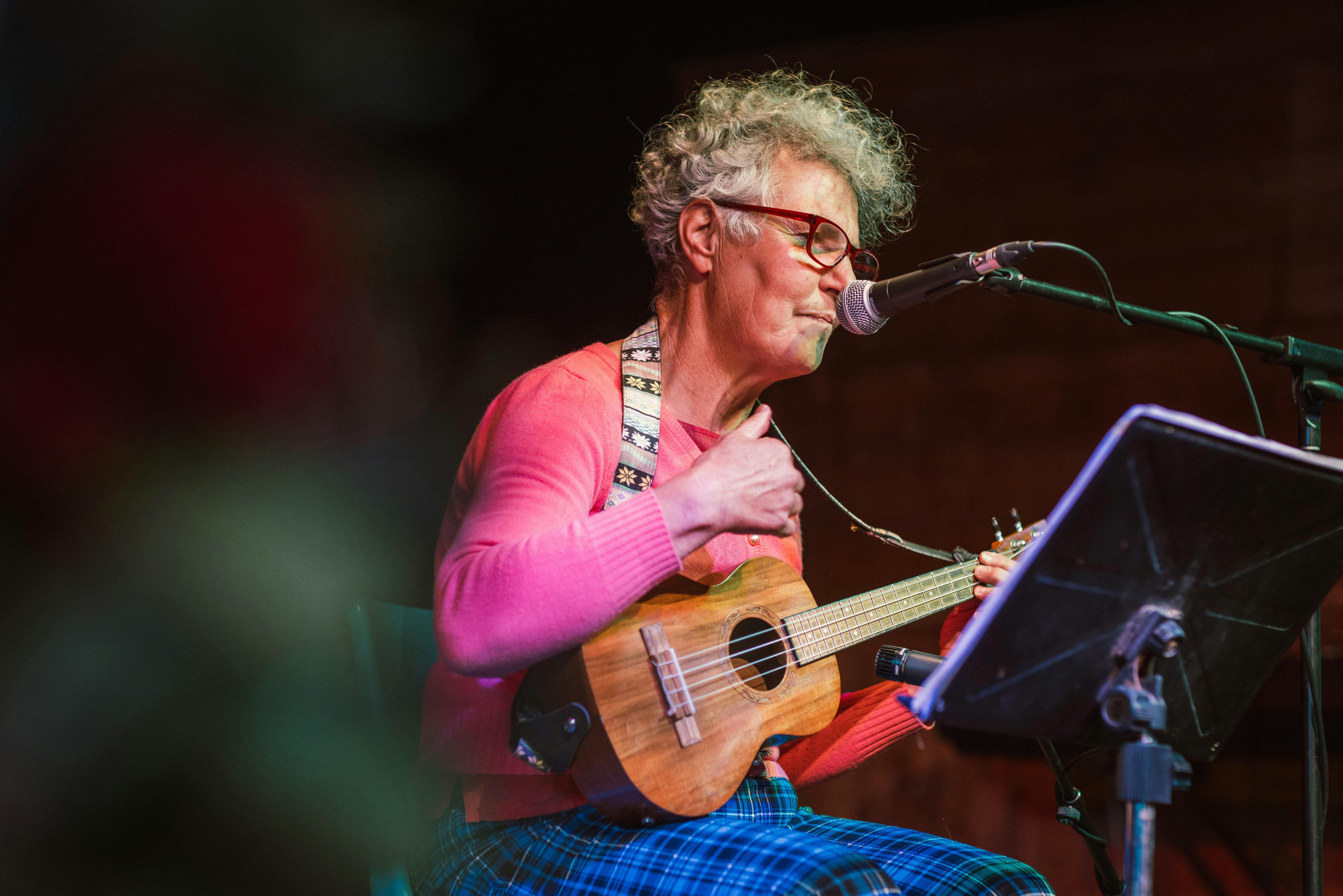 A woman is sitting on stage, playing the ukulele.