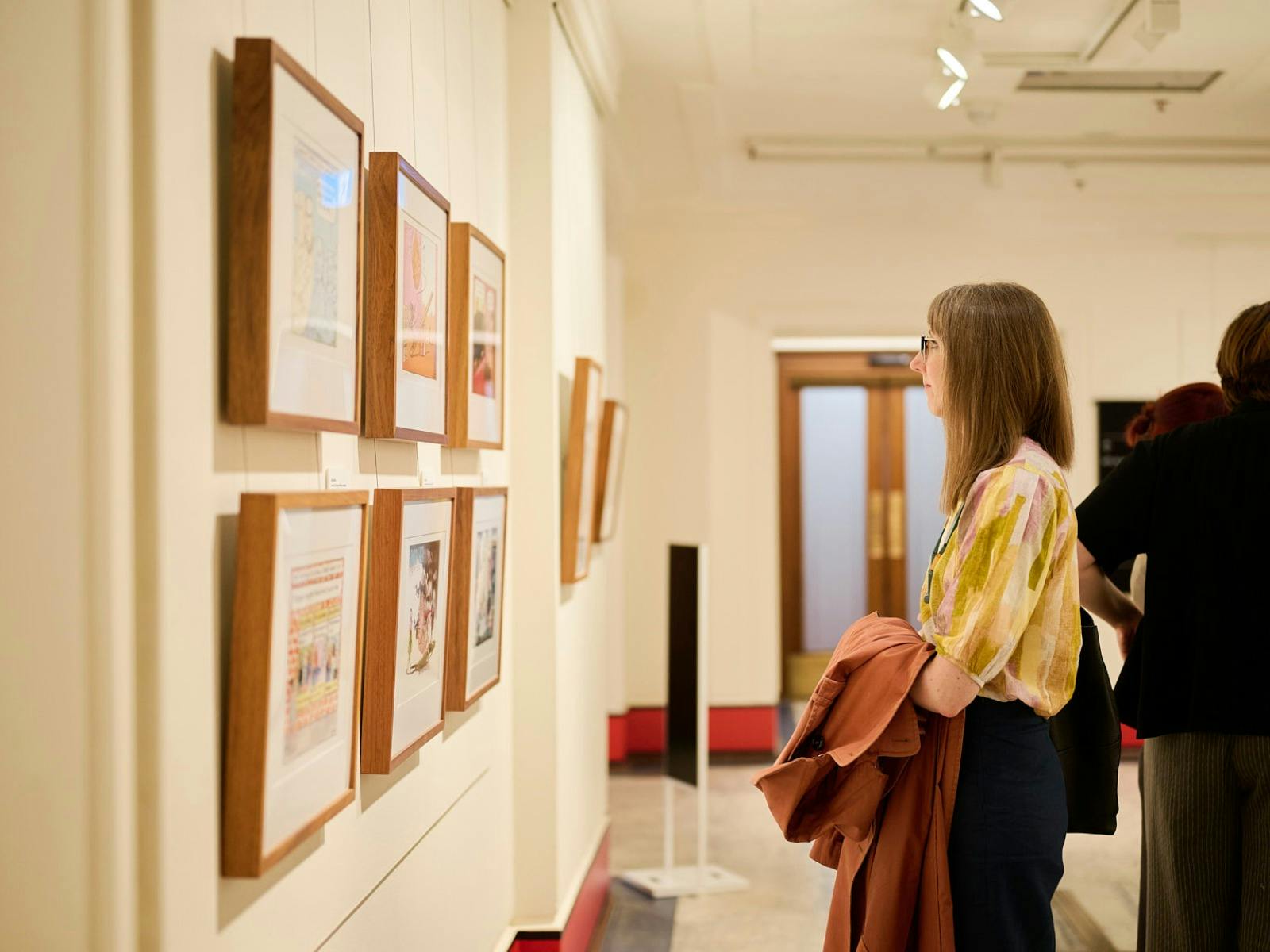 Woman views framed political cartoon in gallery.