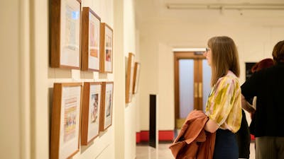 Woman views framed political cartoon in gallery.