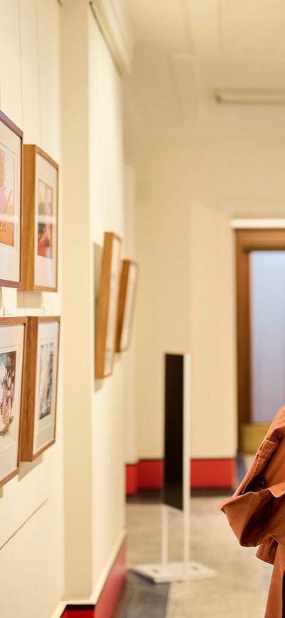 Woman views framed political cartoon in gallery.