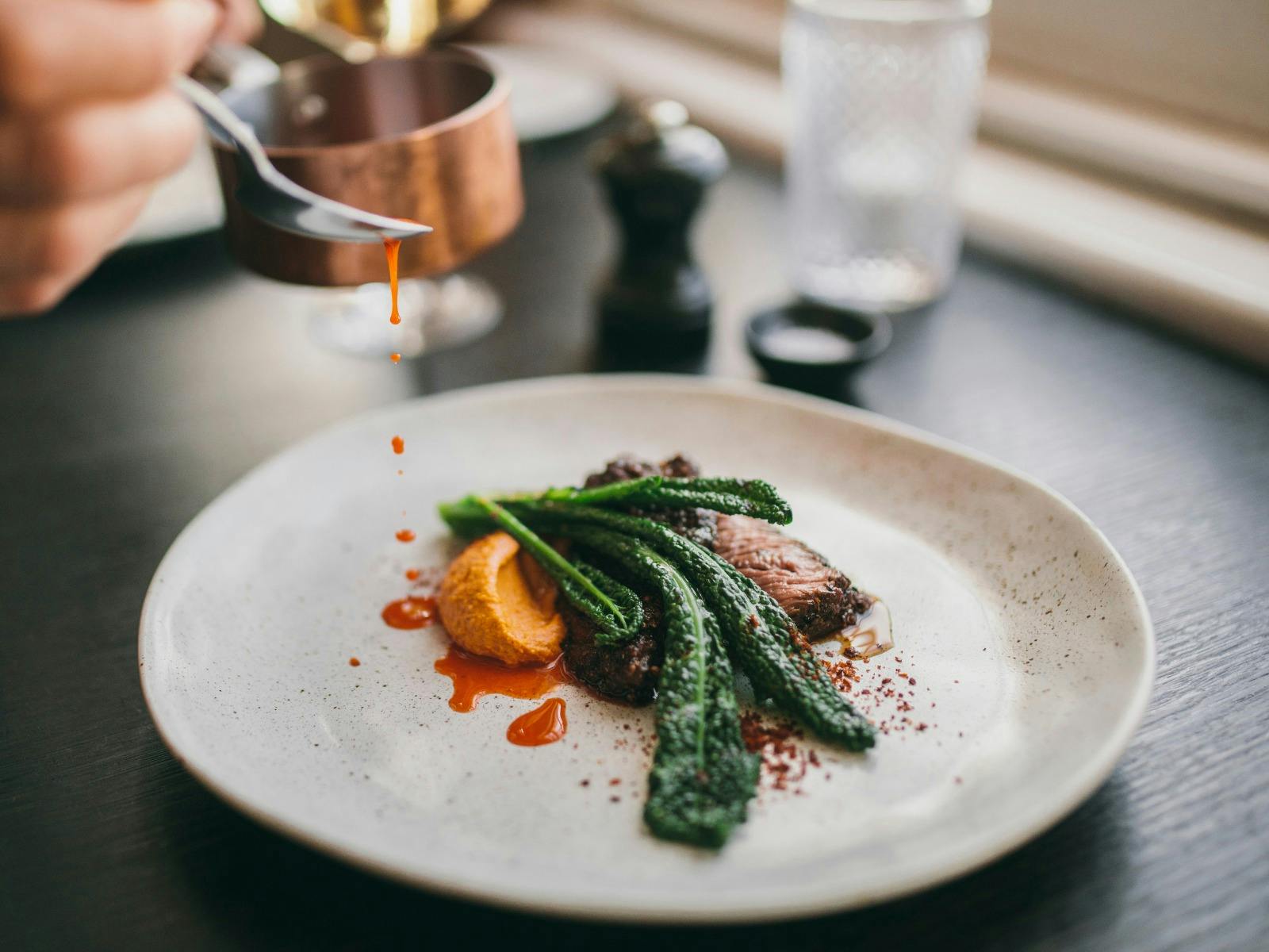 A chef finishing off a main dish with sauce at the table