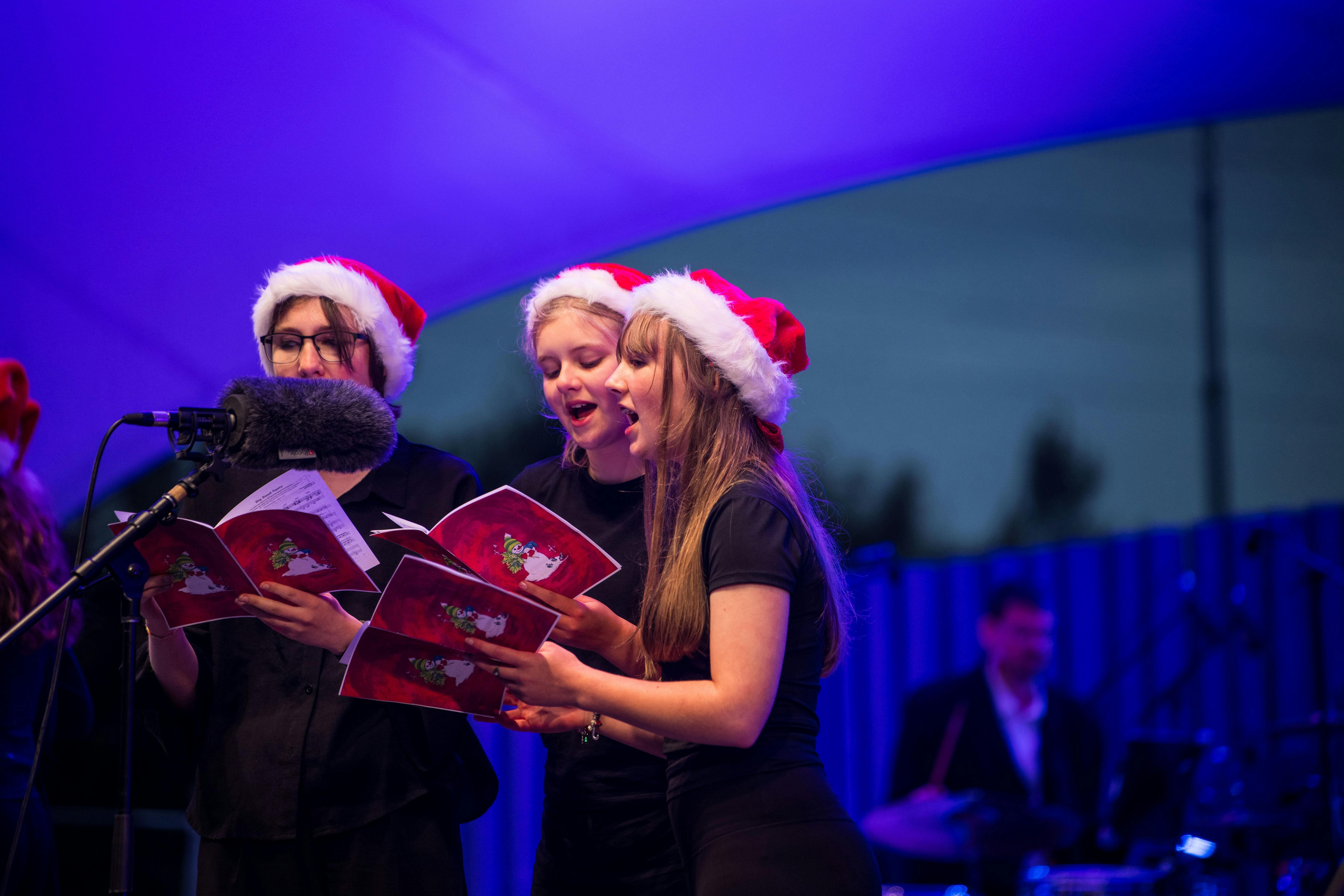 three young women with santa hats carolling