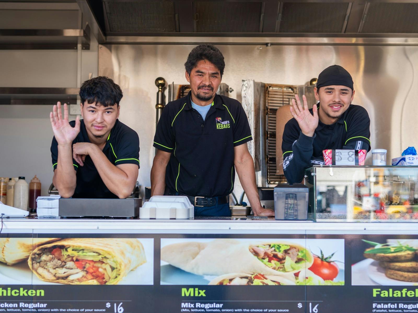 Three workers prepare and serve food from a busy Agfest food van with customers waiting.