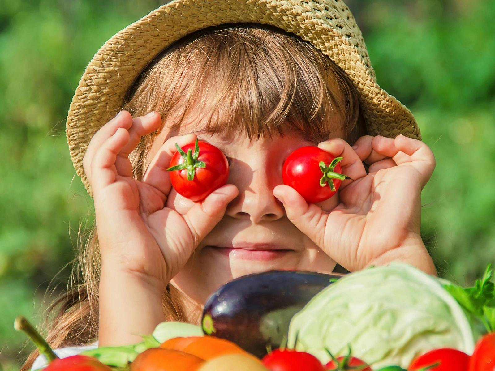 Girl in veggue garden, holding cherry tomotoes over eyes