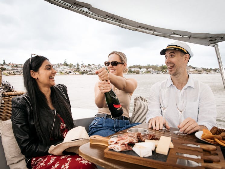 Three people sit on a GoBoat with a bottle of champagne