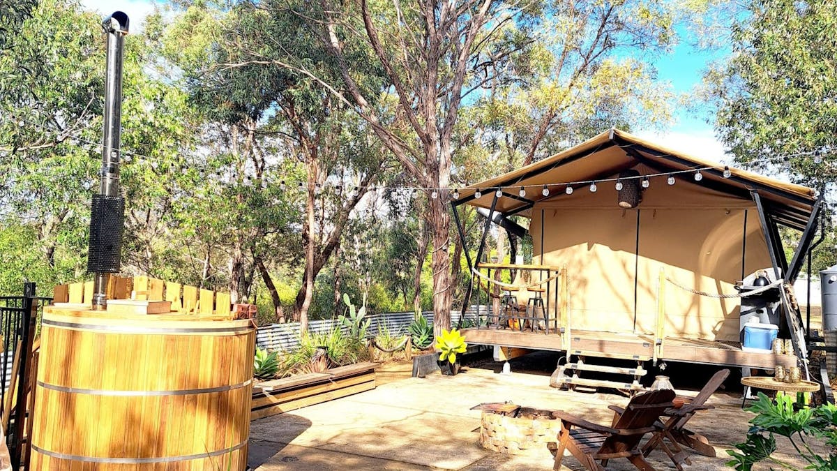 sarafi canvas tent set in bush with a round wooden hot tub with chimmney in foreground