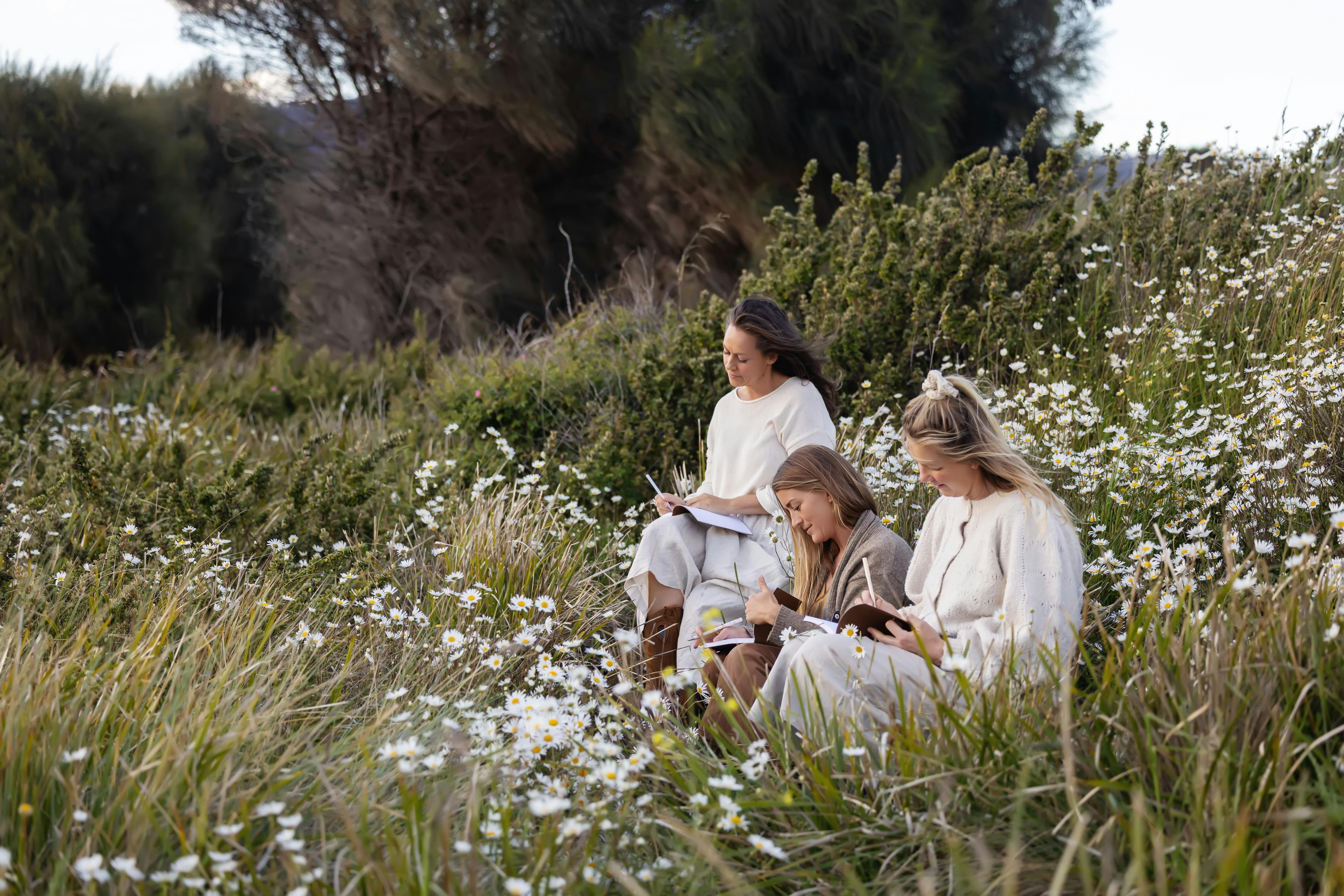 An image of three women sitting amongst wildflowers writing in journals