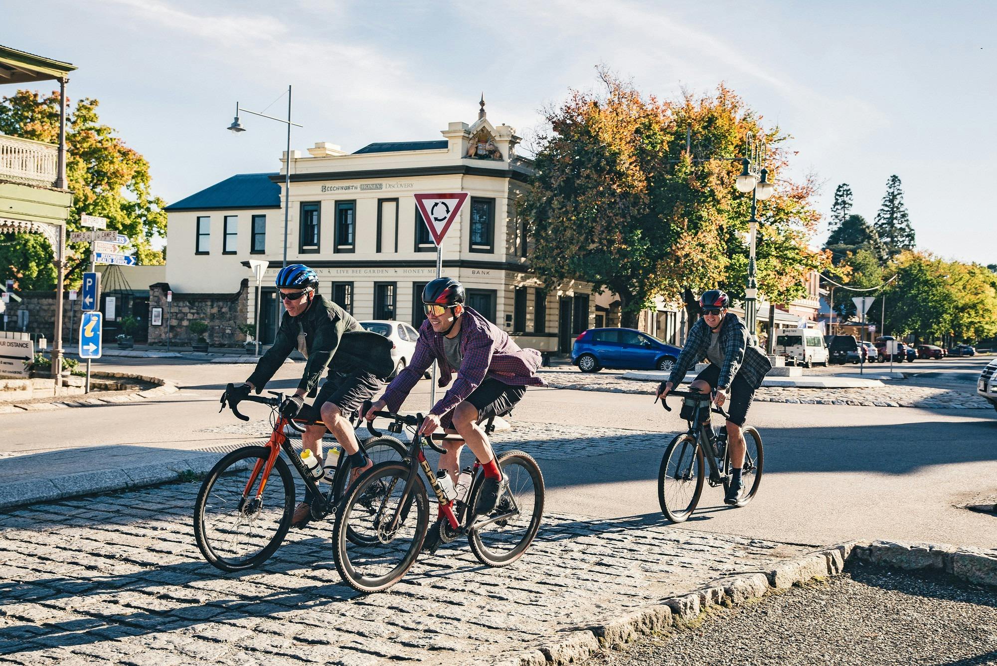 Three gravel cyclists riding past a historic roundabout, an old building and an autumnal tree