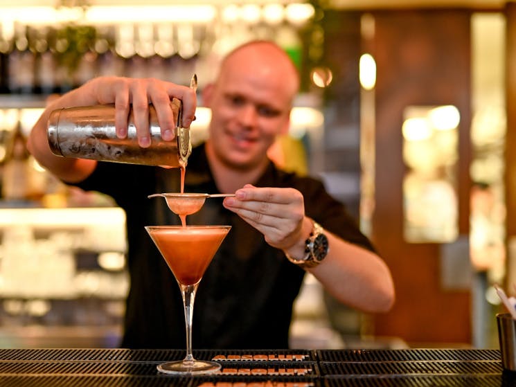 Happy bartender pouring an espresso martini cocktail with the bar as the backdrop