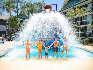 Family standing under the bucket of the junior waterpark at Paradise Resort Gold Coast Family standing under the bucket of the junior waterpark at Paradise Resort Gold Coast