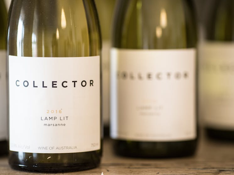 White wine bottles are lined up. The label reads, Collector, Lamp Lit Marsanne 2016.