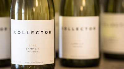 White wine bottles are lined up. The label reads, Collector, Lamp Lit Marsanne 2016.