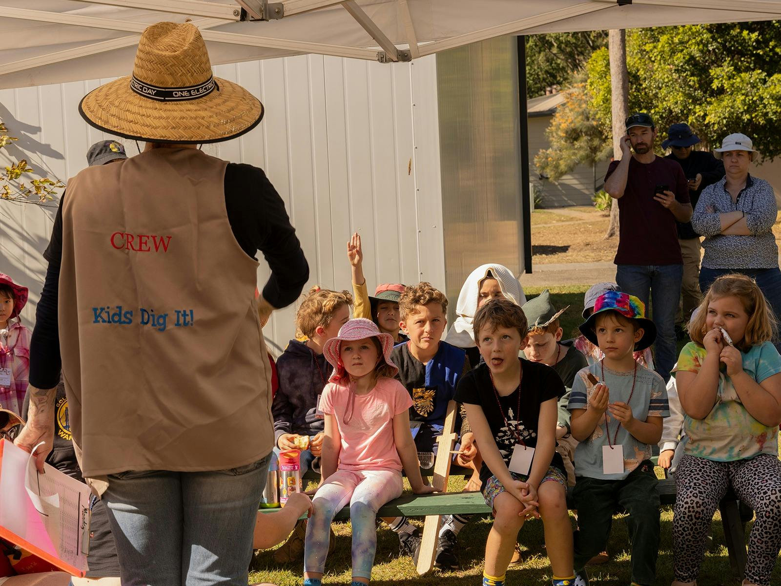Group of children sitting and listening to Educator for instruction outside the Archaeology dig.