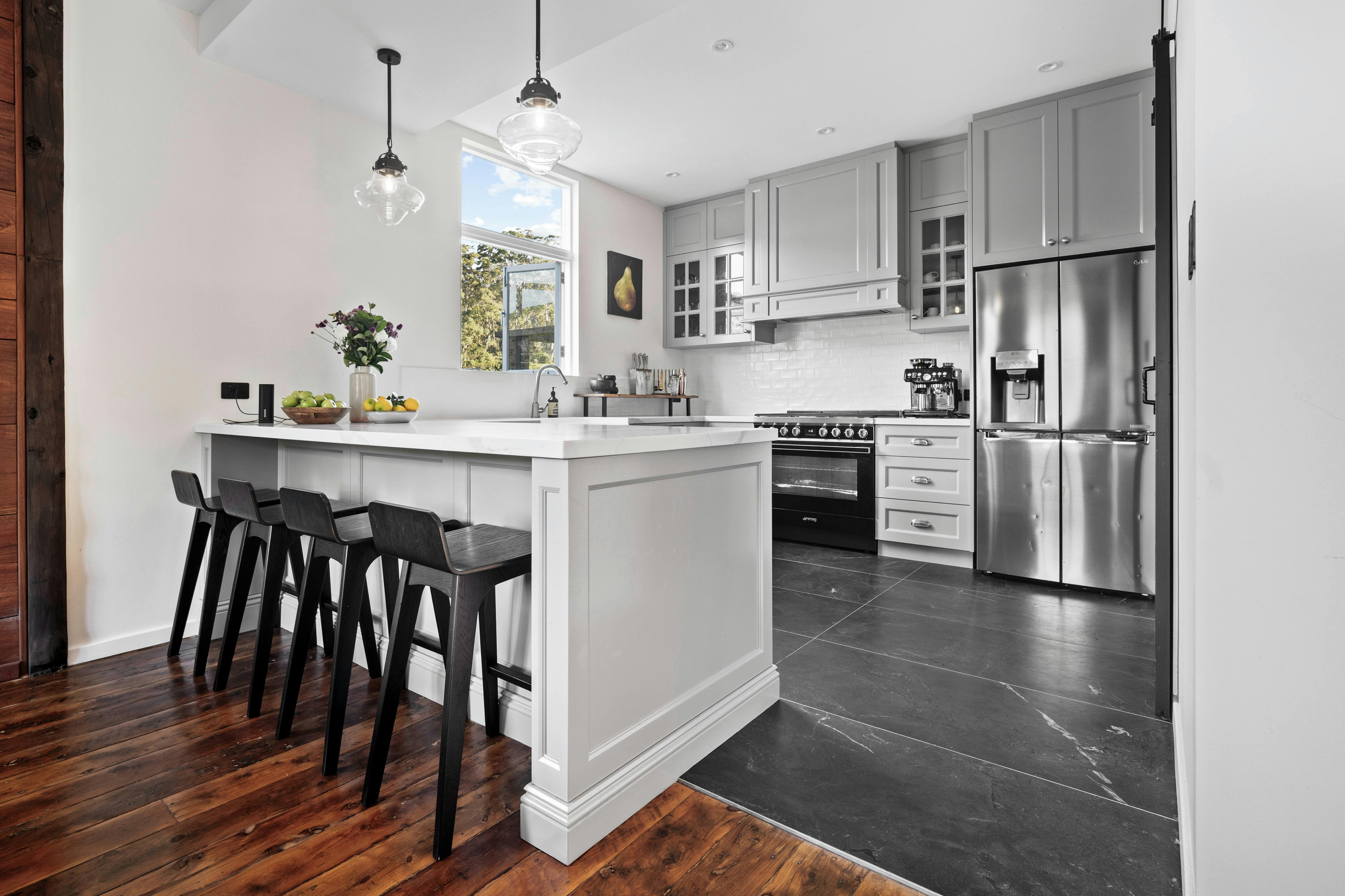 An image of a kitchen island bench with stools, stove, fridge and window overlooking the country