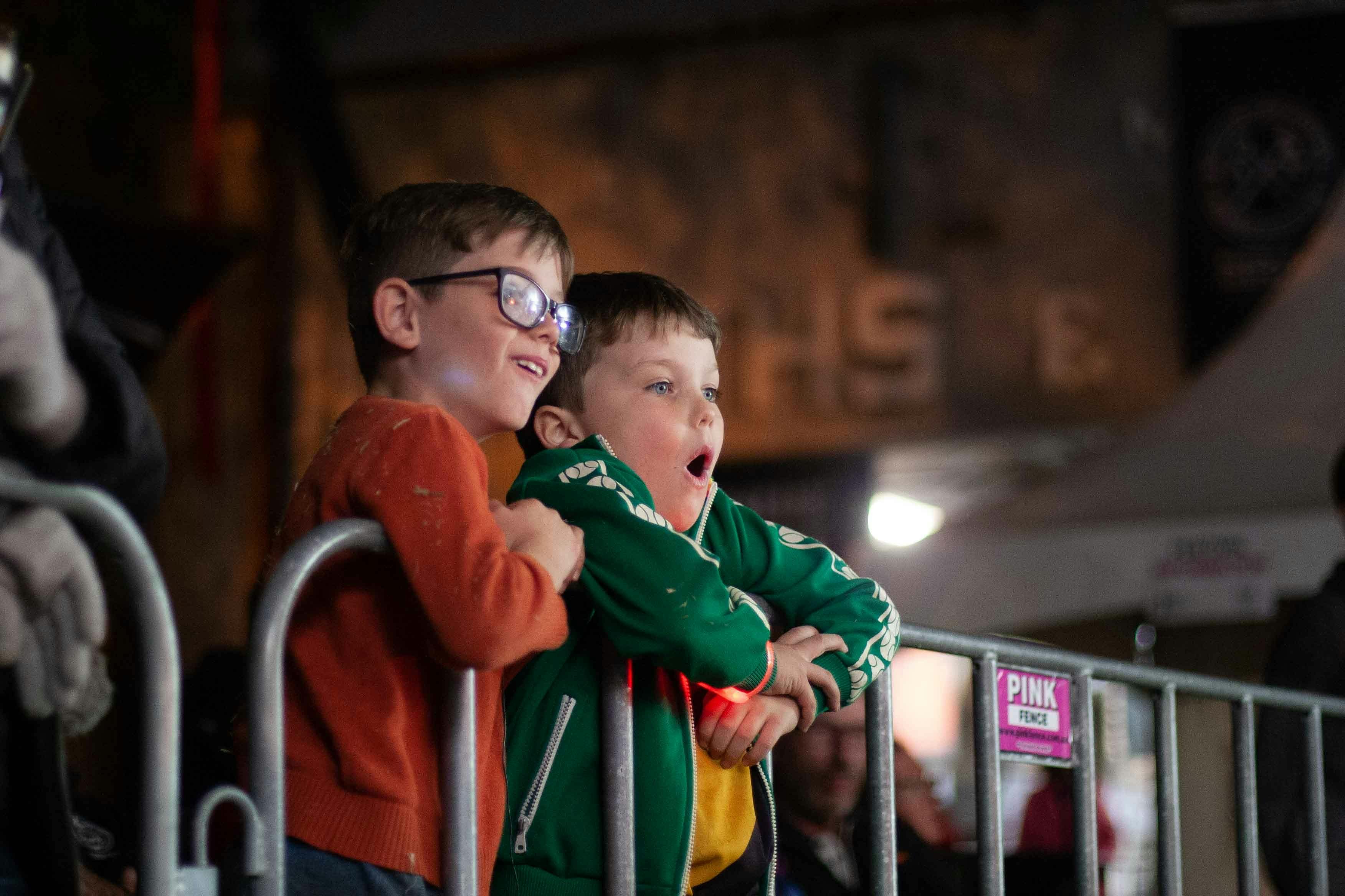 Two children watching a blacksmithing demonstration with wide eyes and excited expressions.