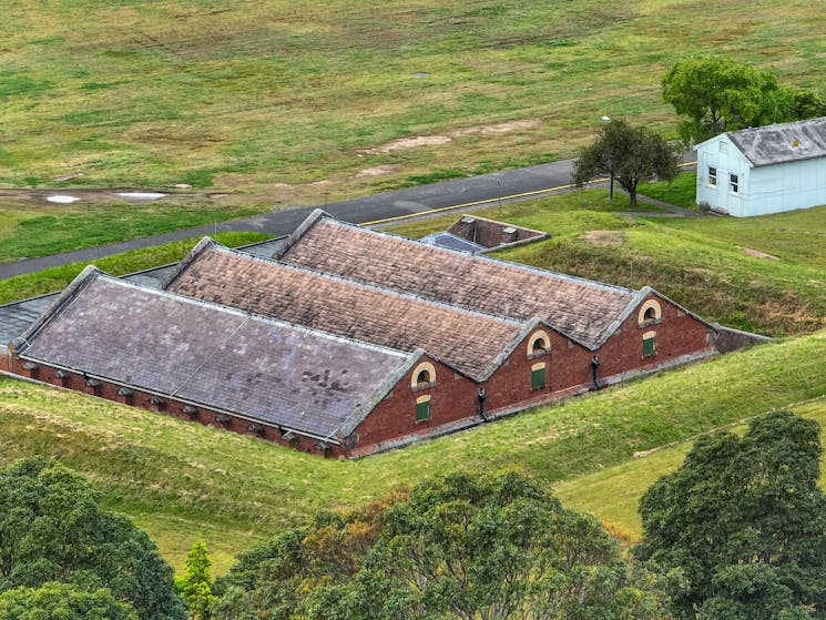 Birds eye, drone view of red brick heritage building with 3 gable roofline, surrounded by grass.