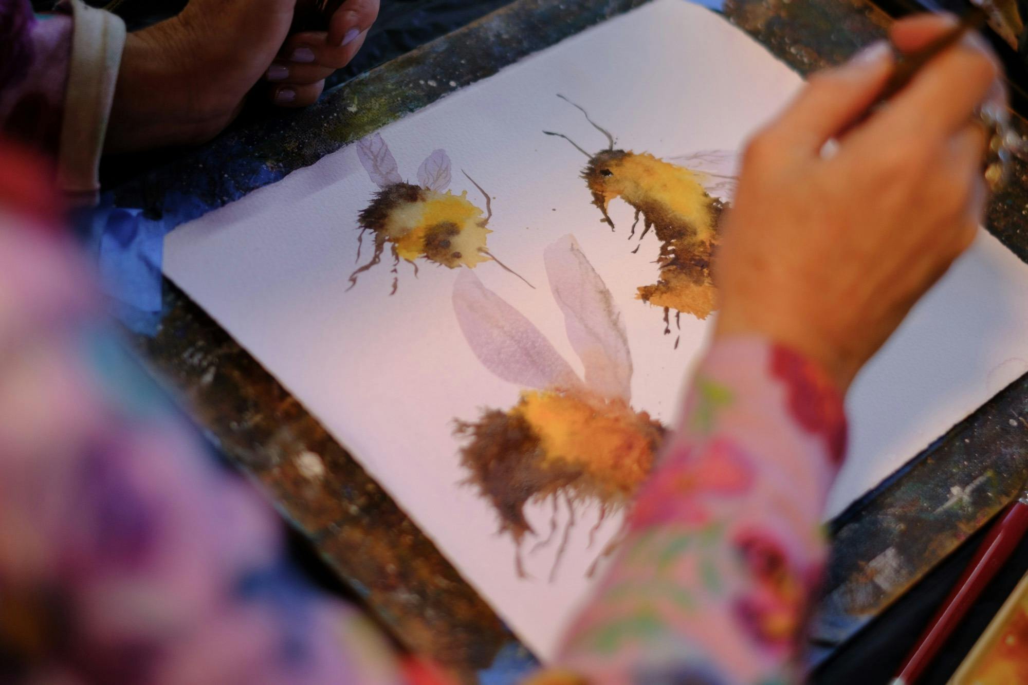 A photograph of a woman making a watercolour painting of bumblebees